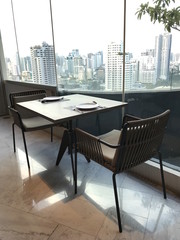 Tablewares, table and chairs for two with cityscape view of buildings in Bangkok.