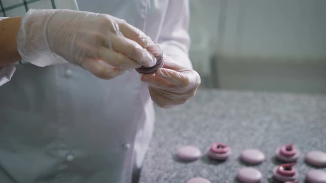 Confectioner connects the two halves of a biscuit between which is a cream. Sweets made by pastry chef in a professional kitchen. Cook makes beautiful desserts with their own hands.
