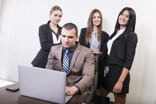Young business man with his assistants. Beautiful woman with standing by a man working on a laptop.