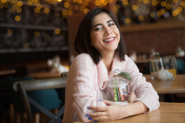 Young beautiful woman with Christmas decor sitting in cafe, drinking coffee. Christmas, new year, winter holidays concept. Christmas morning.

