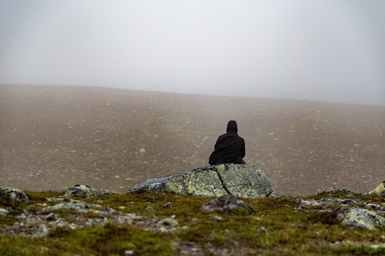 Man in black jacket sits on rock