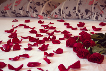 bouquet from red roses and his scattered petals on a bed