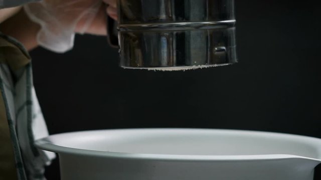 Tearoom in the kitchen. Preparation france makaroons dessert. Woman misses almond flour through a sieve. Using fine sieve is sifted flour mandelic, it should not be larger particles.