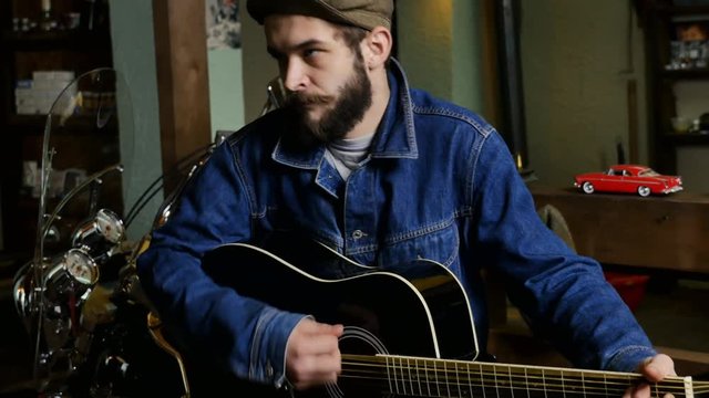 Guitar player playing in a garage in the cap and denim shirt. Music on a stringed instrument in the basement