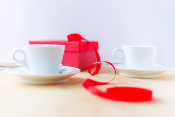 Cups with coffee, gift box, decorated by ribbon on wooden table.