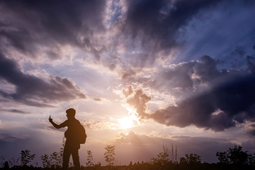 Obraz premium Silhouette man with backpack use smartphone in hands at sunset b