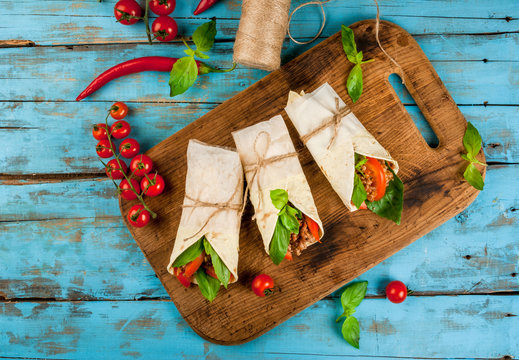 Healthy lunch snack. Sandwiches twisted roll Tortilla with beef and vegetables a wooden cutting board on blue wooden rustic table, copy space, top view