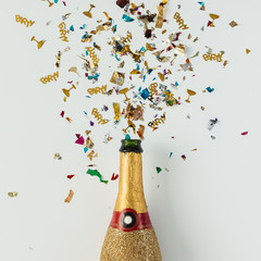 Golden champagne party bottle with confetti on bright background