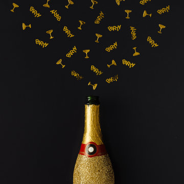 Golden champagne party bottle with confetti on dark background.