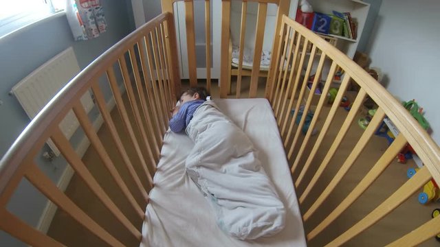 Little toddler boy falling to sleep in his cot but tossing and turning as he is fighting sleep.  Filmed in a time lapse shot.