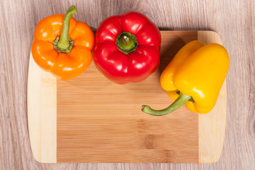 Three colors the peppers on wood cutting background. Yellow, orange and red peppers. Popular pepper in kitchen.