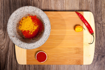Stone mortar with paprika powder. Spices on cutting board whit hot chili and Habanero. Culinary composition on wood table background.