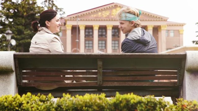 Mother and son sitting on the city park bench and have funny conversation 