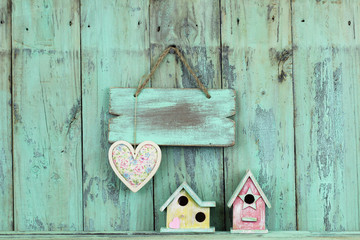 Blank wood sign with heart hanging over colorful birdhouses