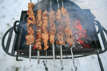 The pork shish kebab on skewers prepares on a brazier in the winter on the backyard.
