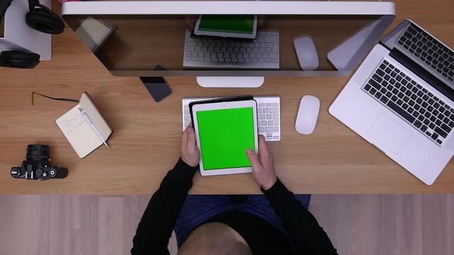Overhead high angle shot of Caucasian worker in casual clothes using his tablet pc In modern office. Green screen, chroma key on tablet
