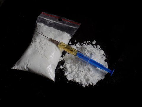 Injection syringe on cocaine drug powder bag and pile on black background