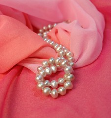 Beads from pearls against the background of pink fabric.