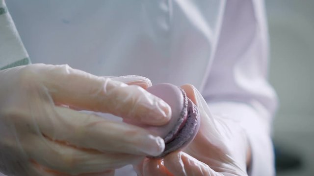 Confectioner connects the two halves of a biscuit between which is a cream. Sweets made by pastry chef in a professional kitchen. Cook makes beautiful desserts with their own hands.