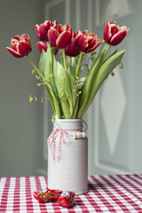 Rot-weisse Tulpen - Tulipa - in einem grauen Krug aus Keramik mit niederlaendischen Holzclogs dekoriert, auf einem Tisch. Farbwelt: gruen, rot, weiss, grau