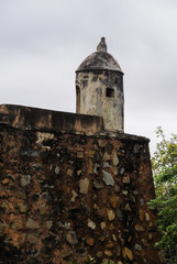 Part of an old fort, with a side of a watchtower over a wall made of stone.