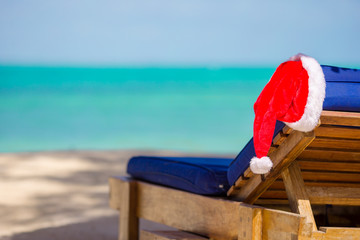 Santa Claus Hat on beach lounger with turquoise sea water and white sand. Christmas vacation concept