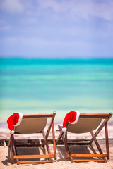 Sun loungers with Santa hat at tropical beach with white sand and turquoise water
