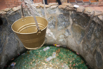 A golden bucket hanging above a little fountain made of stone.