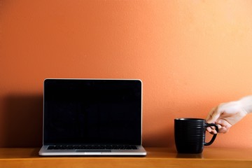 Hand Setting Mug Next to Laptop over Orange Background - 131844437