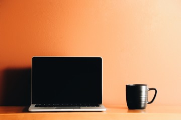 Mug Next to Laptop over Orange Background - 131844487