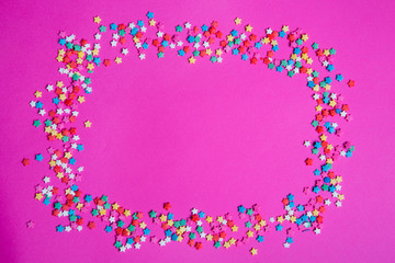Small star candies on a pink background. Various color sprinkles scattered.

