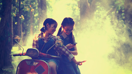 Asian children are sitting on the motorcycle and playing on smart phone with vintage color filter and soft focus