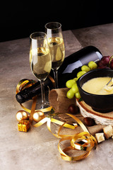 Gourmet Swiss fondue dinner on a winter evening with assorted cheeses on a board alongside a heated pot of cheese fondue with two forks dipping bread and white wine behind in a tavern or restaurant