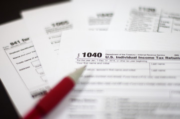 Tax Season: Horizontal left side view of 1040 U.S. Individual Income Tax Return Form with an office laptop background with red white pen and eye glasses foreground