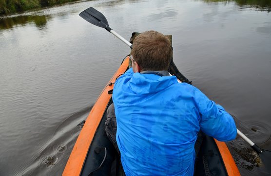 Мужчина в синей куртке гребет на надувной лодке на реке