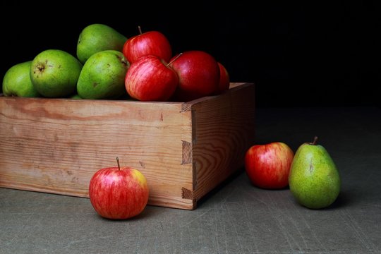 Red, green, sweet pear and an apple in an old wooden box on a dark background