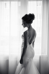 Silhouette of a beautiful bride in a traditional white wedding dress, stood by window.
