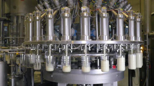 Milk pouring into bottles on a industrial equipment at a milk production factory. 4K.