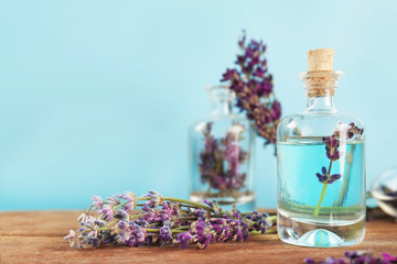 Obraz na płótnie Canvas Bottles with lavender oil and flowers on blue background