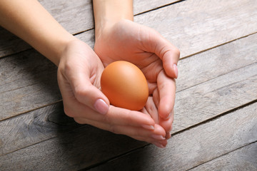 Woman holding raw egg on wooden background