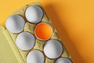 Raw eggs in package on color background