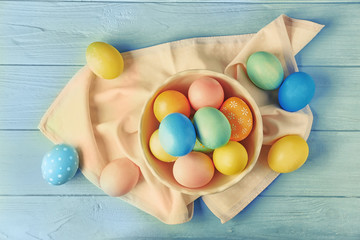 Fototapeta na wymiar Bowl with colourful Easter eggs and napkin on blue wooden table