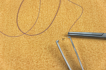 Needle holder holding fine needle with purple suture and surgical tweezer in front of skin...