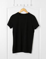Naklejka premium Pusta czarna koszulka wisząca na białych drzwiach