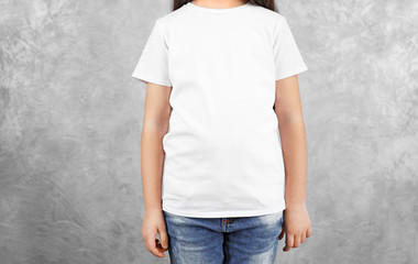 Little girl in blank white t-shirt standing against grey textured wall, close up