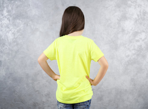 Little girl in blank color t-shirt standing against grey textured wall