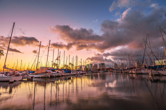 Dramatic landscape of sailing boats and yachts docked at the Ala Wai Harbor, the largest yacht harbor of Hawaii, reflecting in the sea at sunset. Honolulu, Oahu, Hawaii.