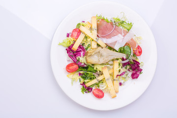 European cuisine dish salad from vegetables, cheese and ham. food on a white plate and a top view of a light background