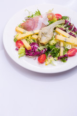 European cuisine dish salad from vegetables, cheese and ham. food on a white plate and a top view of a light background