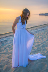 Fototapeta na wymiar Beautiful girl in a long white dress walking on the seaside.